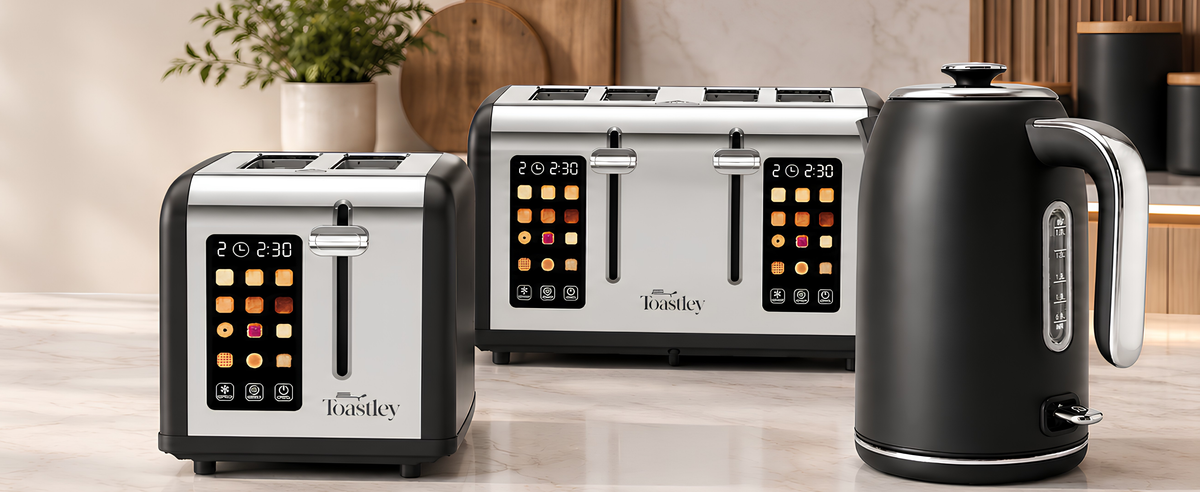 A kitchen countertop setup featuring a black and stainless steel 4-slice toaster, a larger matching 4-slice toaster behind it, and a black electric kettle on a light stone surface. The toasters and kettle have touch-screen controls and the Tousetley brand name is visible on the front.