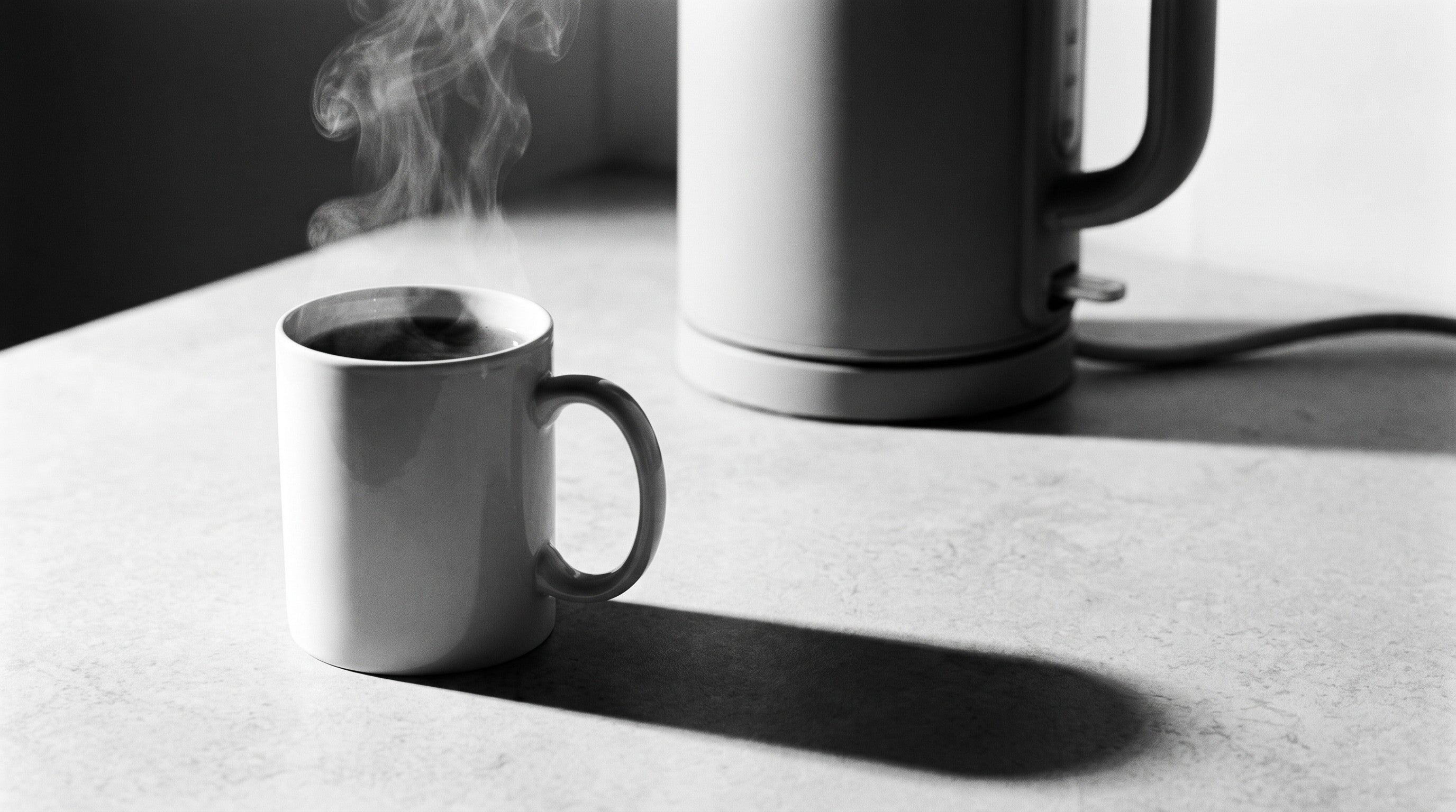 Image of A single white mug of freshly poured black tea steaming on a kitchen worktop, with a cordless electric kettle on its power base softly out of focus behind