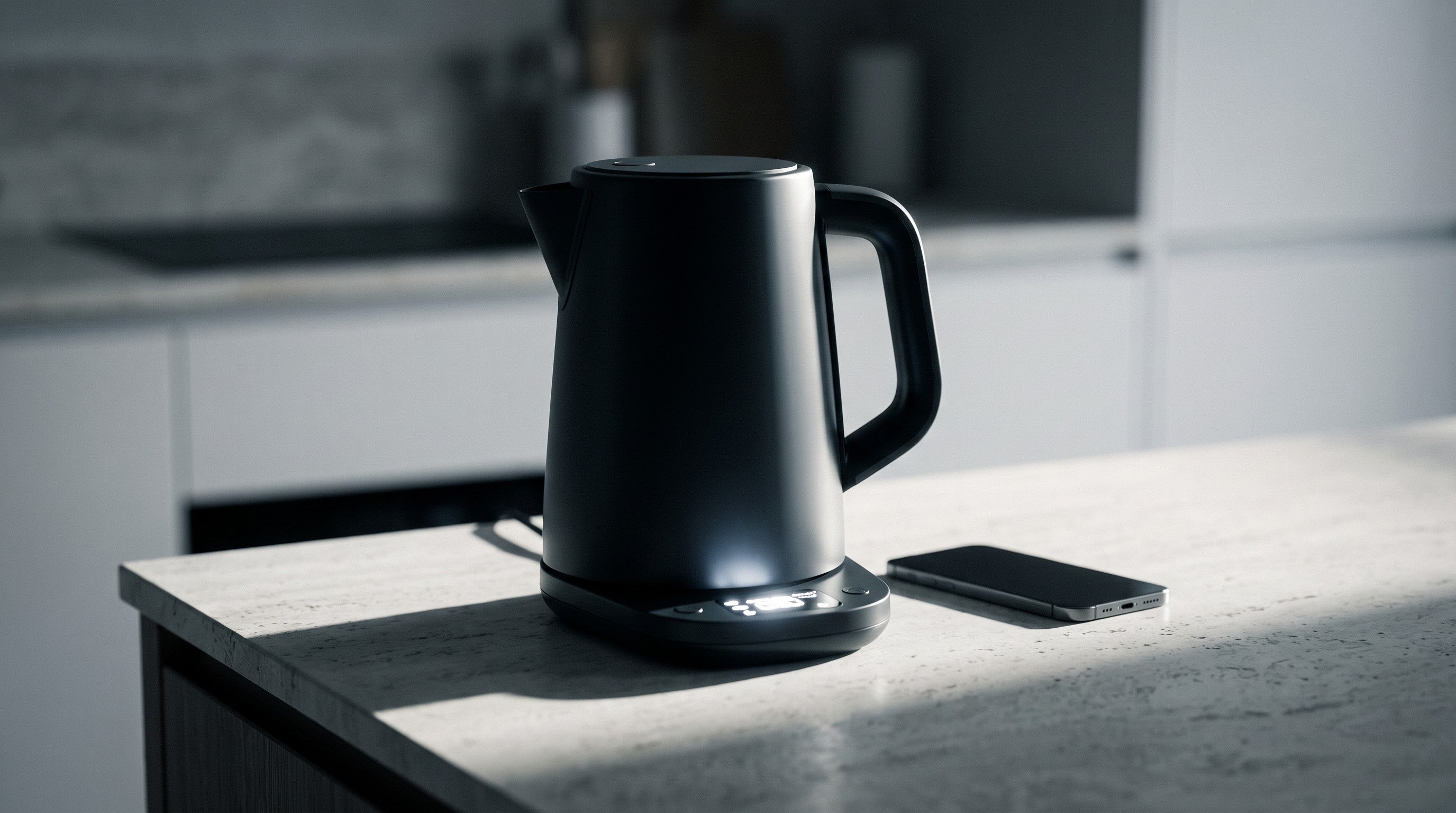 Image of A matt black electric kettle on a dim kitchen worktop with a small illuminated control display glowing on its base, a phone lying beside it