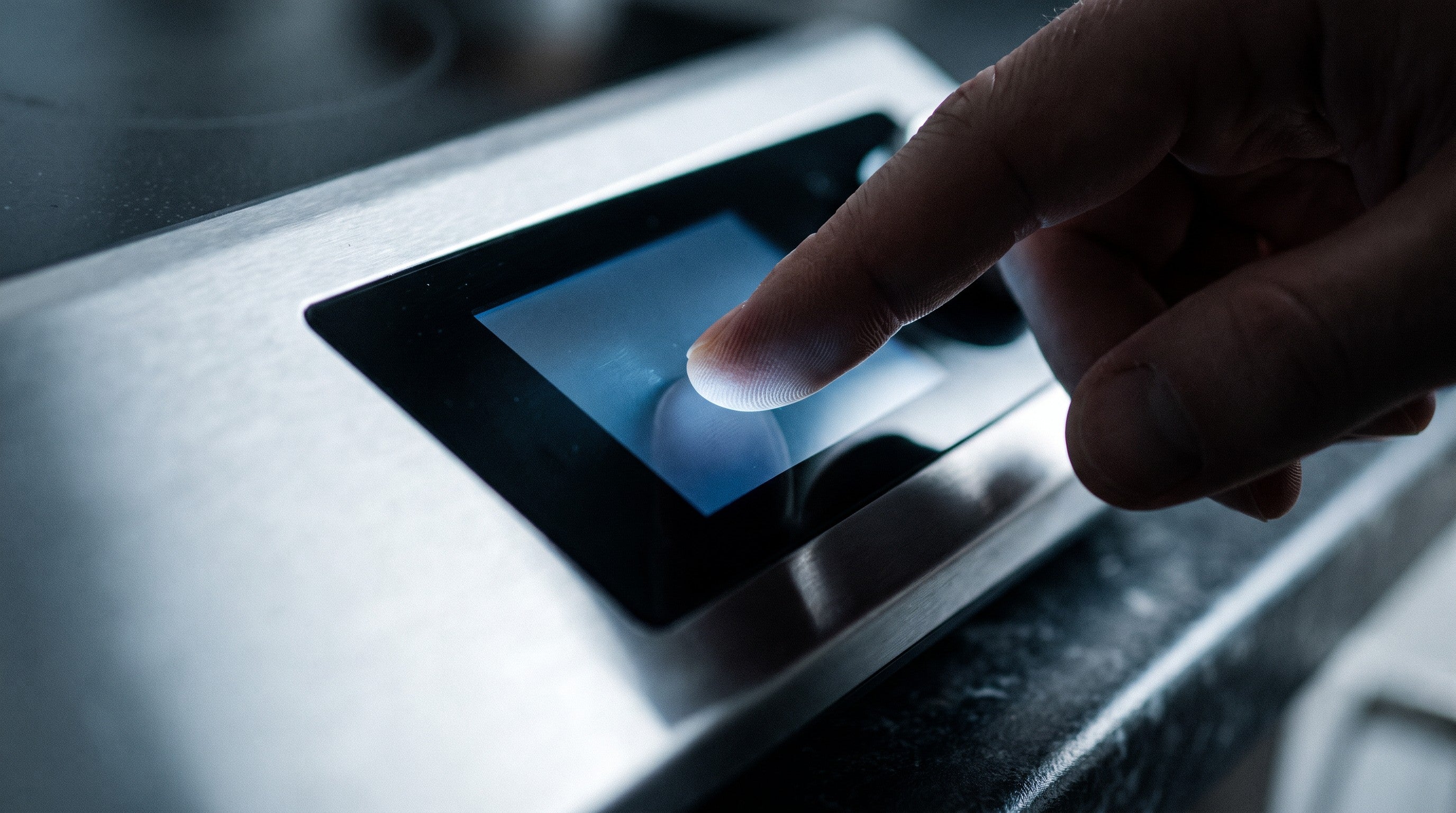 Image of A fingertip pressing a glowing backlit touchscreen control panel on a stainless steel kitchen appliance in a dimly lit kitchen