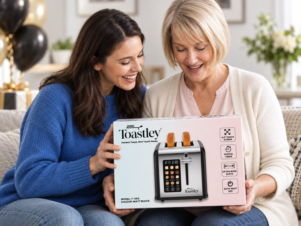 Two women on a sofa with balloons behind them, smiling at a boxed Toastley 2 slice smart toaster in matt black being opened as a gift